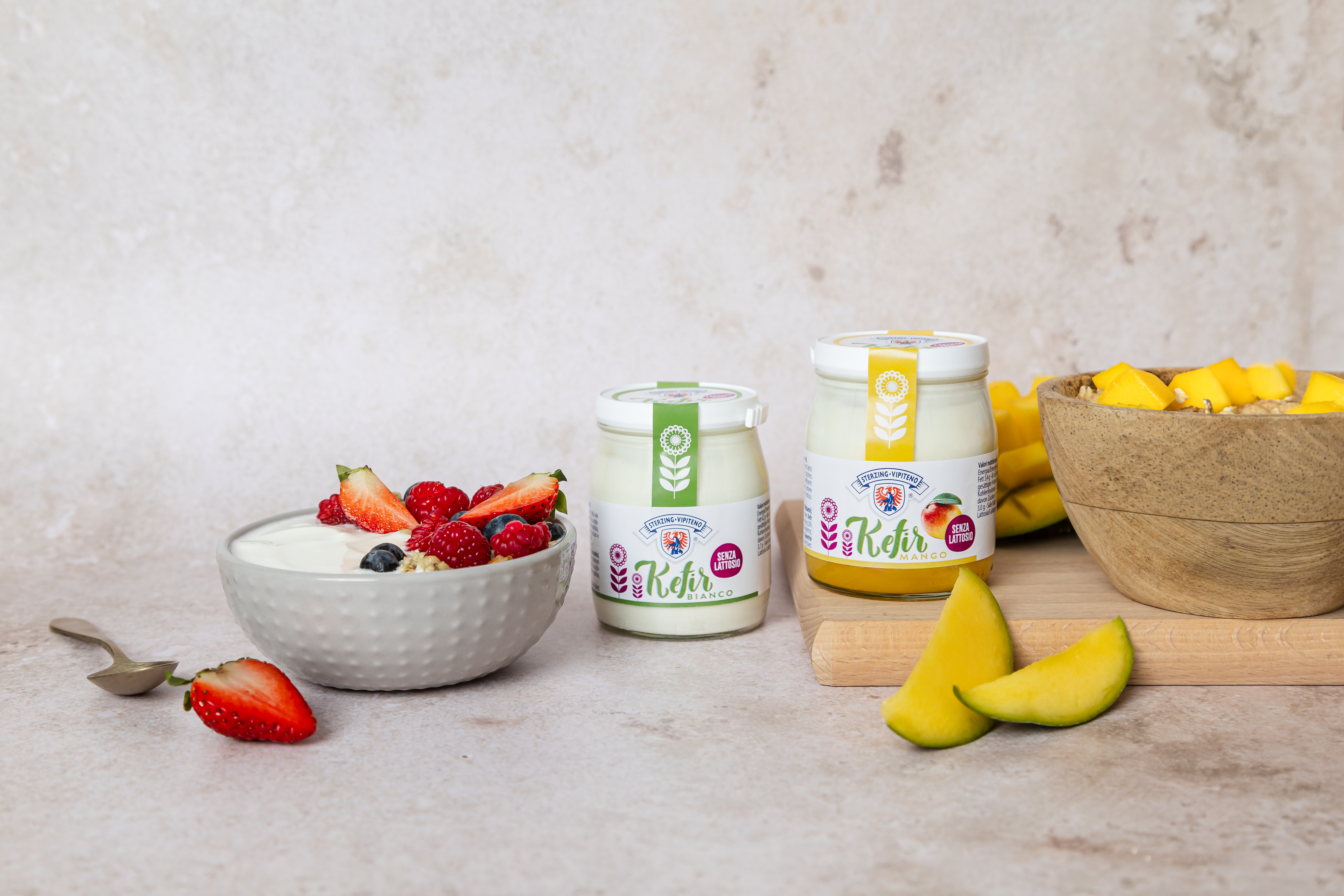 Foto del prodotto: kefir naturale e kefir al mango. Sfondo marmorizzato. La foto è impreziosita da mango e fragole fresche.