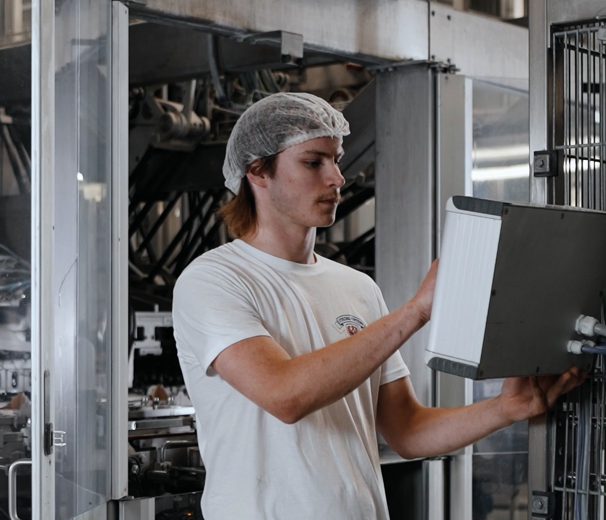 Produktionsmitarbeiter mit Haarnetz bedient ein Bedienpanel an einer Maschine