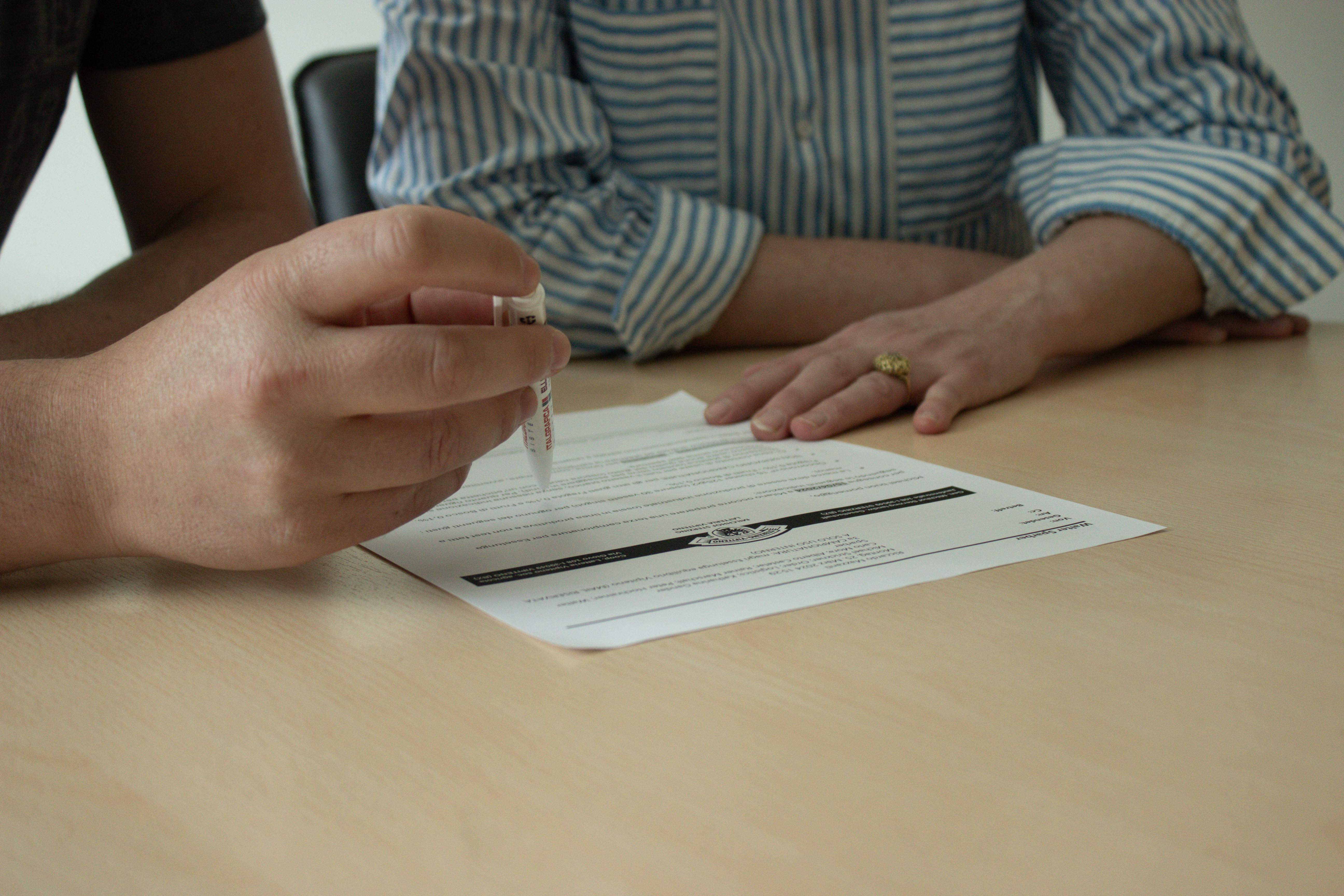 Person hält einen Stift über ein Dokument während eines Gesprächs mit einer anderen Person