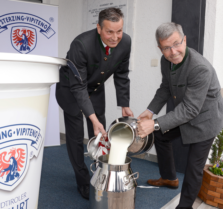 Obmann Adalbert Braunhofer und Anton Steixner leeren gemeinsam Milch in eine Milchkanne.