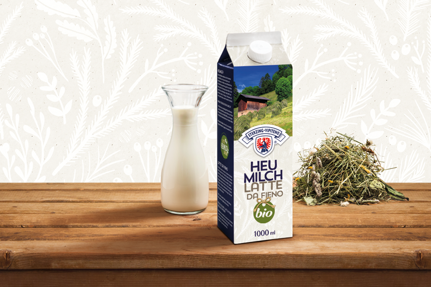 Ursprüngliche Bio Heumilch Verpackung von Milchhof Sterzing mit Milchkaraffe und Heu auf Holztisch