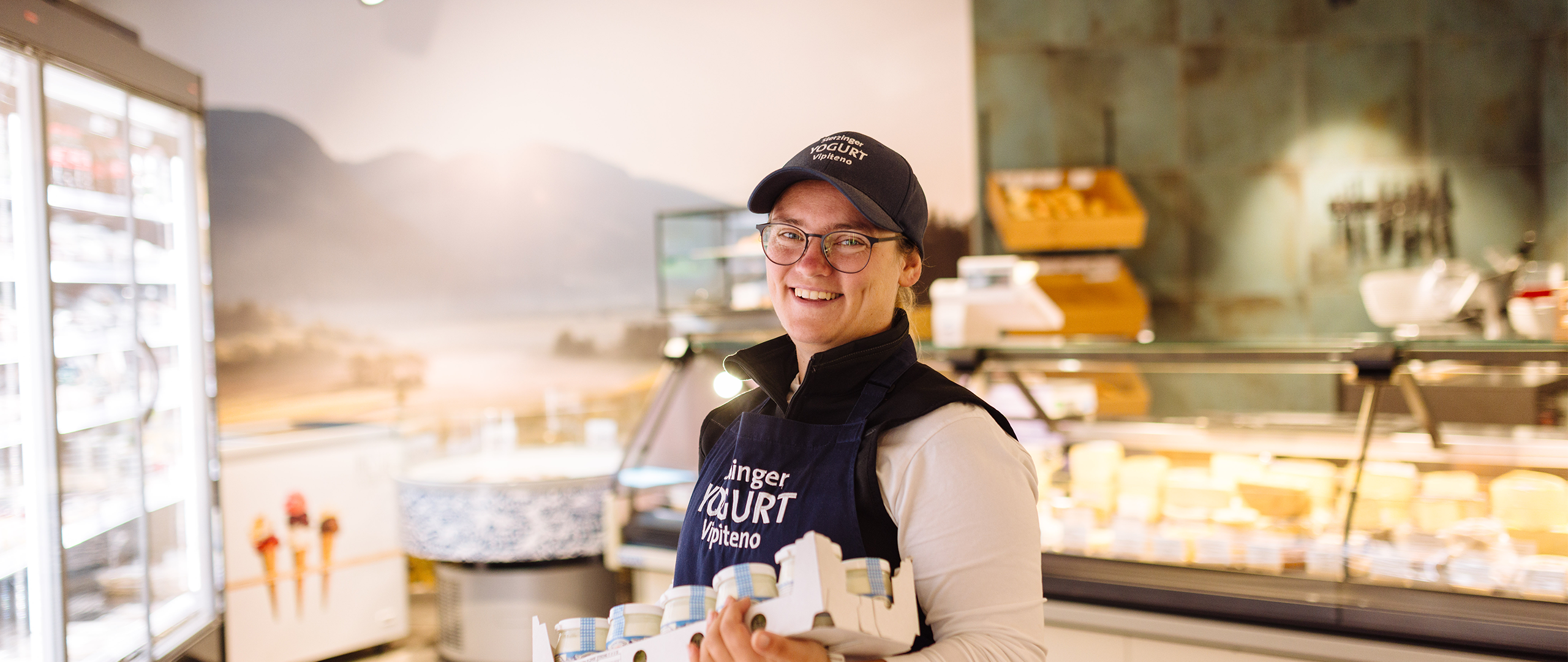 Verkäuferin im Geschäft mit Karton Joghurt in der Hand.